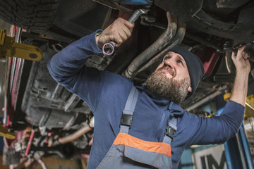 A bearded car mechanic works in the garage. Car mechanic in the garage. Hard work.