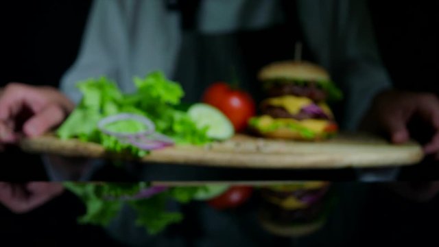 Fresh vegetables and tasty burger with cheese and beef cutlets. Chef on the background out of focus