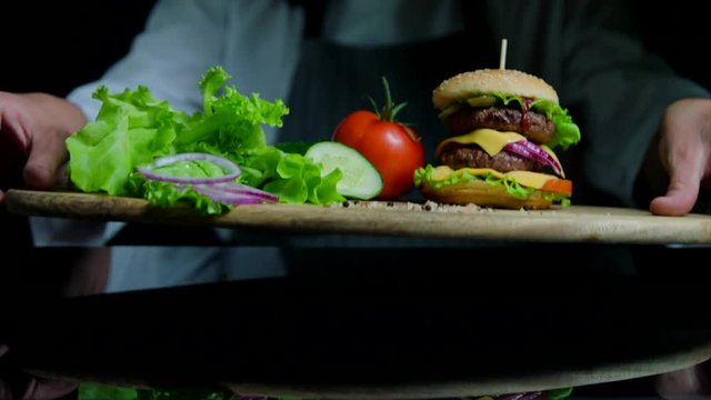 Fresh vegetables and tasty burger with cheese and beef cutlets. Chef on the background out of focus