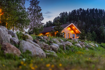 House in the forest. Cottage on the background of stones. Evening landscape with a house. The light burns in the houses.