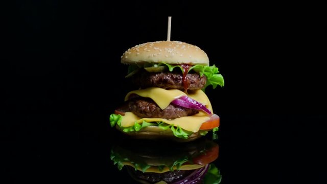 Tasty burger with beef, cheese and greens on the black glass background for commercial