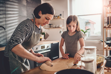 Mother and daughter kneading dough on the wooden table