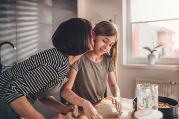 Mother kissing daughter while they making apple pie