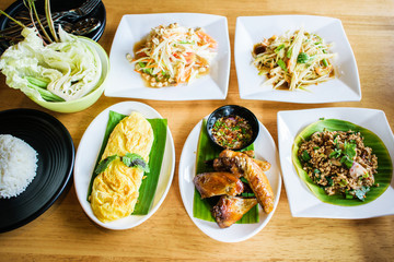 Thai Northeast food; spicy papaya salad, ground pork salad, grilled chicken wings, omelet, cooked rice and fresh vegetable.