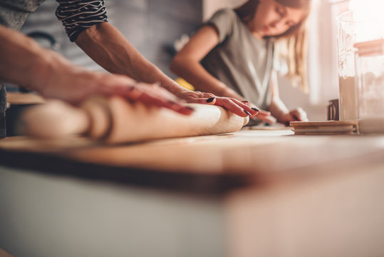 Mother and daughter rolling dough on wooden table