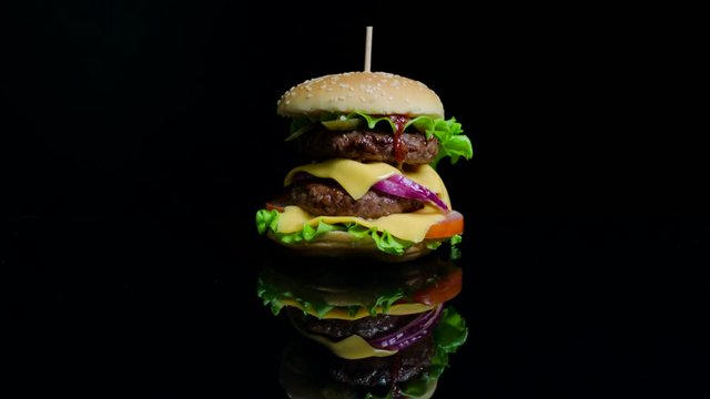 Tasty burger with beef, cheese and greens on the black glass background for commercial