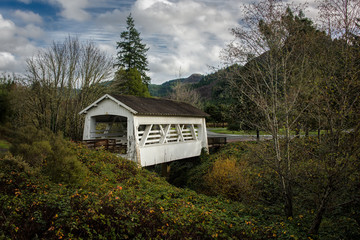 White covered bridge with trees, green foliage and beautiful sky.