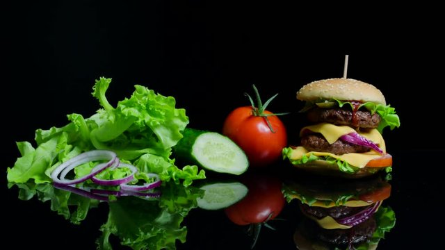 Fresh vegetables and tasty burger with cheese and beef cutlets on the black background