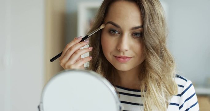 Close up of the charming youg woman doing makeup for herself as being beauty blogger. Indoors.