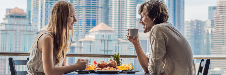 Loving couple having breakfast on the balcony. Breakfast table with coffee fruit and bread croisant on a balcony against the backdrop of the big city BANNER long format