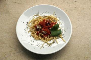 Spaghetti with meatballs in a tomato sauce, served in a white plate, restaurant, close up, focus