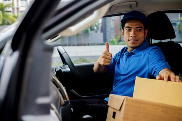 Delivery driver driving van with parcels on seat outside warehouse