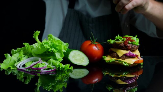 Chef finishing the savory burger with beef, cheese and vegetables. Black background for commercial