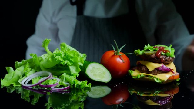 Chef finishing the savory burger with beef, cheese and vegetables. Black background for commercial