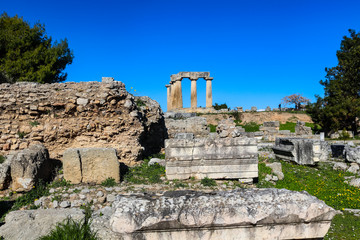 Temple of Apollo in ancient Corinth Greece viewed from down the hll in the excavated ruins with unidentifiable tourists taking pictures up above and yellow flowers in bloom