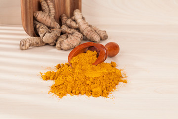 Turmeric powder and fresh turmeric on wooden background