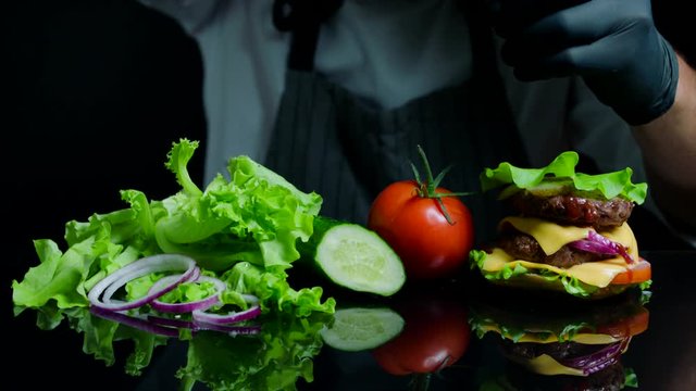 Chef finishing the savory burger with beef, cheese and vegetables. Black background for commercial