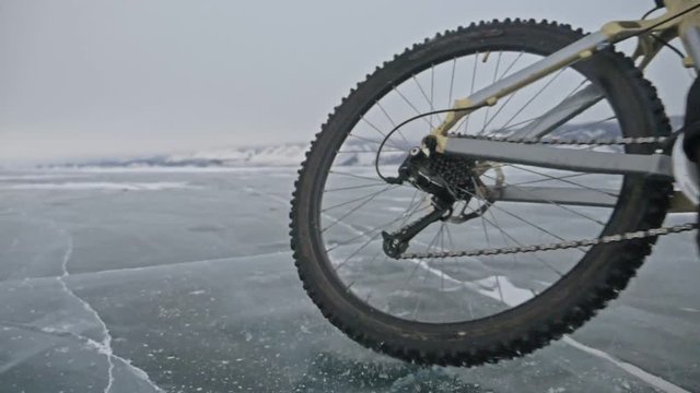 View of tire. Shooting 180fps. Man is riding bicycle on the ice. The cyclist cuts in front of the camera. Pieces of ice fly in us. Ice of the frozen Lake Baikal. The tires on the bicycle are covered