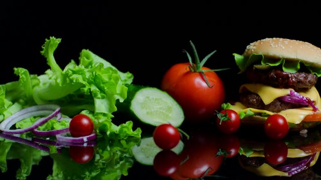 Fresh vegetables and tasty burger with cheese and beef cutlets on the black background