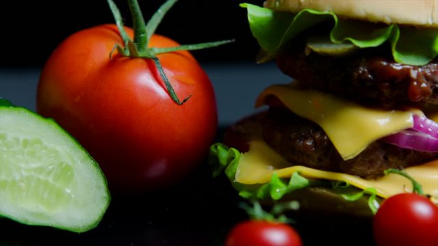Close up of fresh vegetables and tasty burger with cheese and beef cutlets on the black background