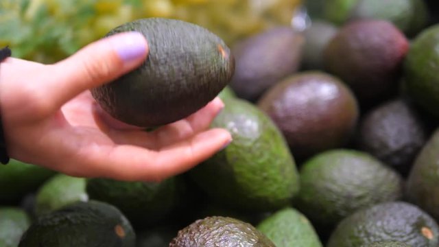 Closeup Of Female Hand Choosing Avocado Fruit On Market