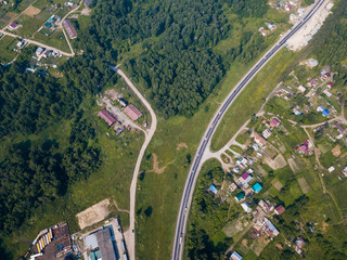 Photographing from a quadrocopter to a large village with small houses, a green forest and a large field on a warm, sunny summer day
