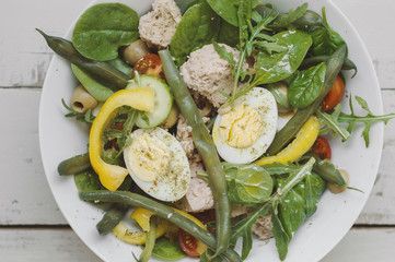 Salad with eggs, tuna, green beans, arugula, spinach, cucumber, cherry tomatoes, yellow bell pepper and olives. View from above