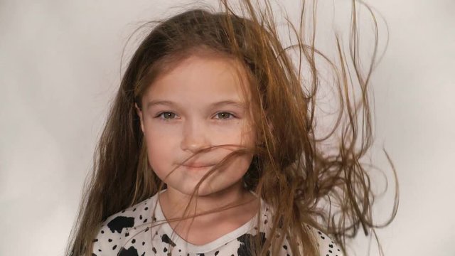 Happy little girl in the studio on a gray background. She jumps, shows different emotions. Hair fluttering from the wind. Super slow motion, shot at 180fps.