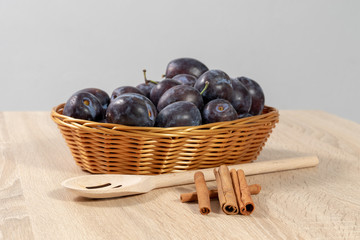 Cinnamon and a wooden spoon  in front of a basket full of ripe plums