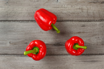 Tabletop view - three red bell peppers on gray wood desk.