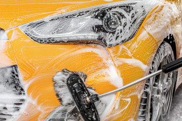 Front headlight and bumper of yellow car being washed in self service carwash, brush leaving...