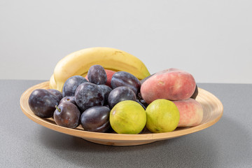 Flat basket full of ripe fruits - plums, bananas, lemons, 