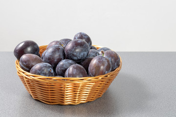 Basket full of ripe plums on a grey table 