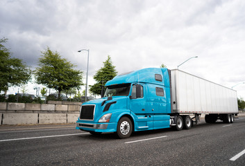 Blue big rig semi truck with dry van semi trailer transporting cargo on the wide multiline highway