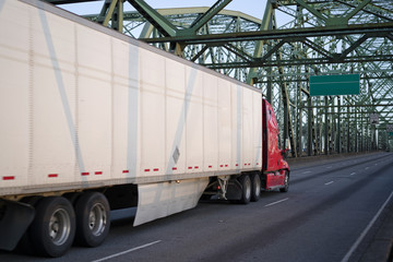 Red big rig semi truck transporting commercial cargo in dry van semi trailer driving on arched metal truss Columbia Interstate bridge