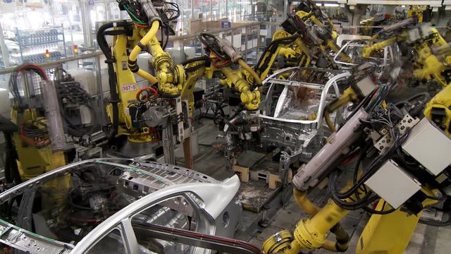The group of robots in an automatic mode perform joint work on assembling and welding of the body of a modern car