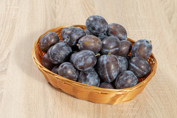 Brown basket full of ripe plums on a wooden table