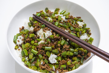 Bowl of minced beef with round beans and rice, with chopsticks on white background