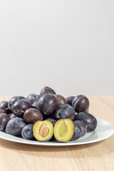 Halved plum with several ripe plums on a white plate in the kitchen 
