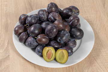 Ripe plums on a white plate in the kitchen on a wooden table 