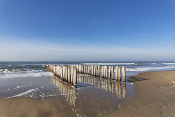 Fototapeta na wymiar Waves at Domburg Beach where the timber piles are reflected in the Water / Netherlands