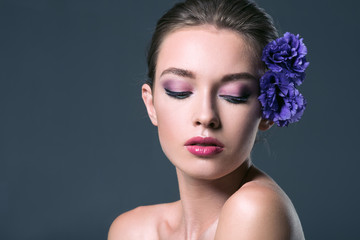 beautiful young woman with eustoma flowers in hair and closed eyes isolated on grey