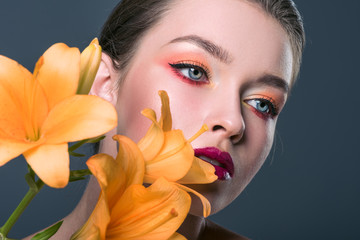 close-up portrait of attractive young woman with fashionable makeup and orange lilium flowers...