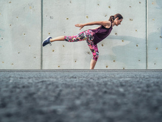 fitness lady making balance Pose outdoor infront of a grey cement wall as background