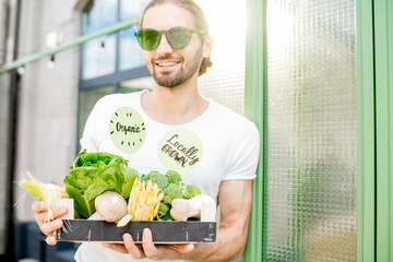 Portrait of a handsome vegetarian man standing with box full of organic vegetables outdoors