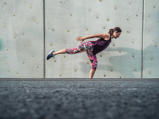 fitness lady making balance Pose outdoor infront of a grey cement wall as background