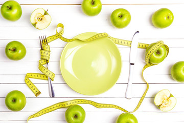 Diet concept table setting with cutlery, yellow measuring tape and green apples on white wooden...