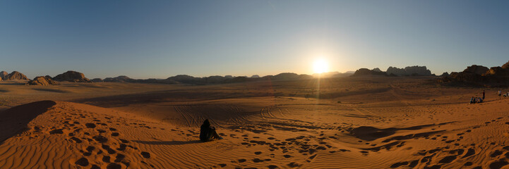 Tourists sit on a sand dune to admire sunset in Wadi Rum desert, Jordan.