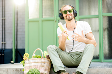 Funny portrait of a man listening to the music and singing with corn sitting with healthy food outdoors
