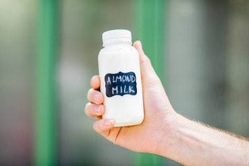 Holding bottle with almond milk with stickers on the green background
